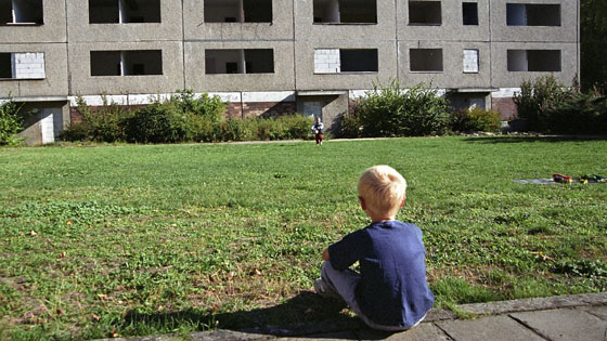 Ein Kind sitzt vor einem leerstehenden Plattenbau