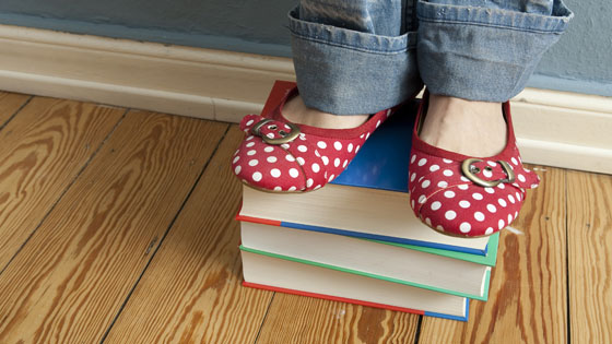 Eine Frau steht in bunten Schuhen auf einem Bücherstapel