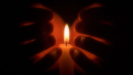 Hände umschließen brennende Kerze